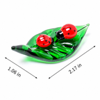 A green leaf-shaped glass candle holder with two red ladybug figures on top, shown on a white background with dimension arrows and labels indicating 1.06 in by 2.