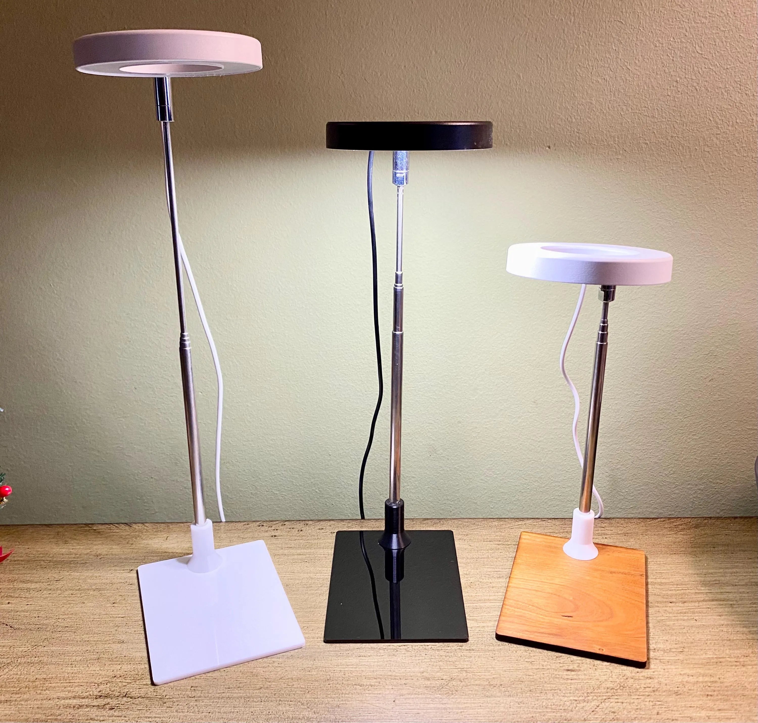 3 adjustable height ring grow lights in bases made of white acrylic, black acrylic and wood